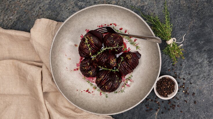 Hasselback-stekte rødbeter på en rustikk tallerken, garnert med frisk timian, servert med sorte pepperkorn i nærheten.