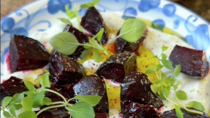 Ovnsbakte rødbeter på kremet pisket ricotta med friske urter, olivenolje og ristede crostini på en blå keramisk tallerken.