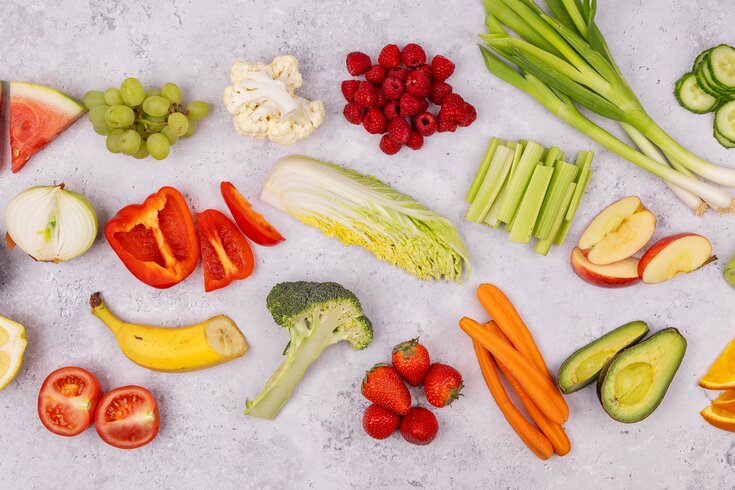 Et fargerikt flatt lag med ferske skivede grønnsaker og frukt, inkludert gulrøtter, brokkoli, jordbær, paprika og agurker.