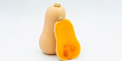 To butternut squash på hvit bakgrunn, en hel og en delt med oransje fruktkjøtt inni.