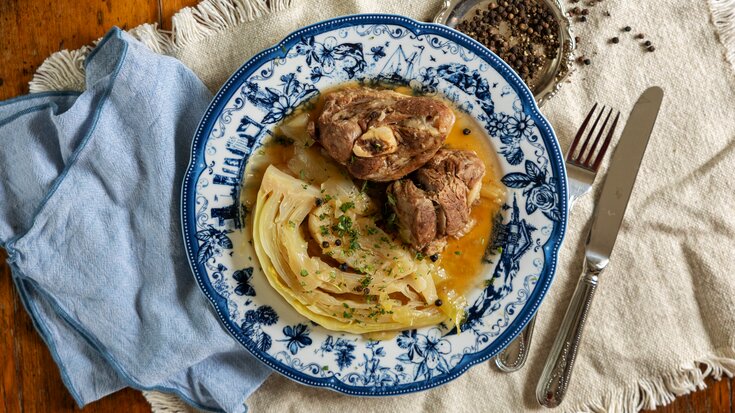 En tallerken med pasta toppet med braisert kjøtt i rik saus, garnert med urter, på et rustikt trebord.