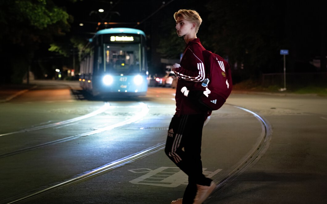 Nattestid  trikk kjører mot gutt med reflekser på vei over sporet. Foto.