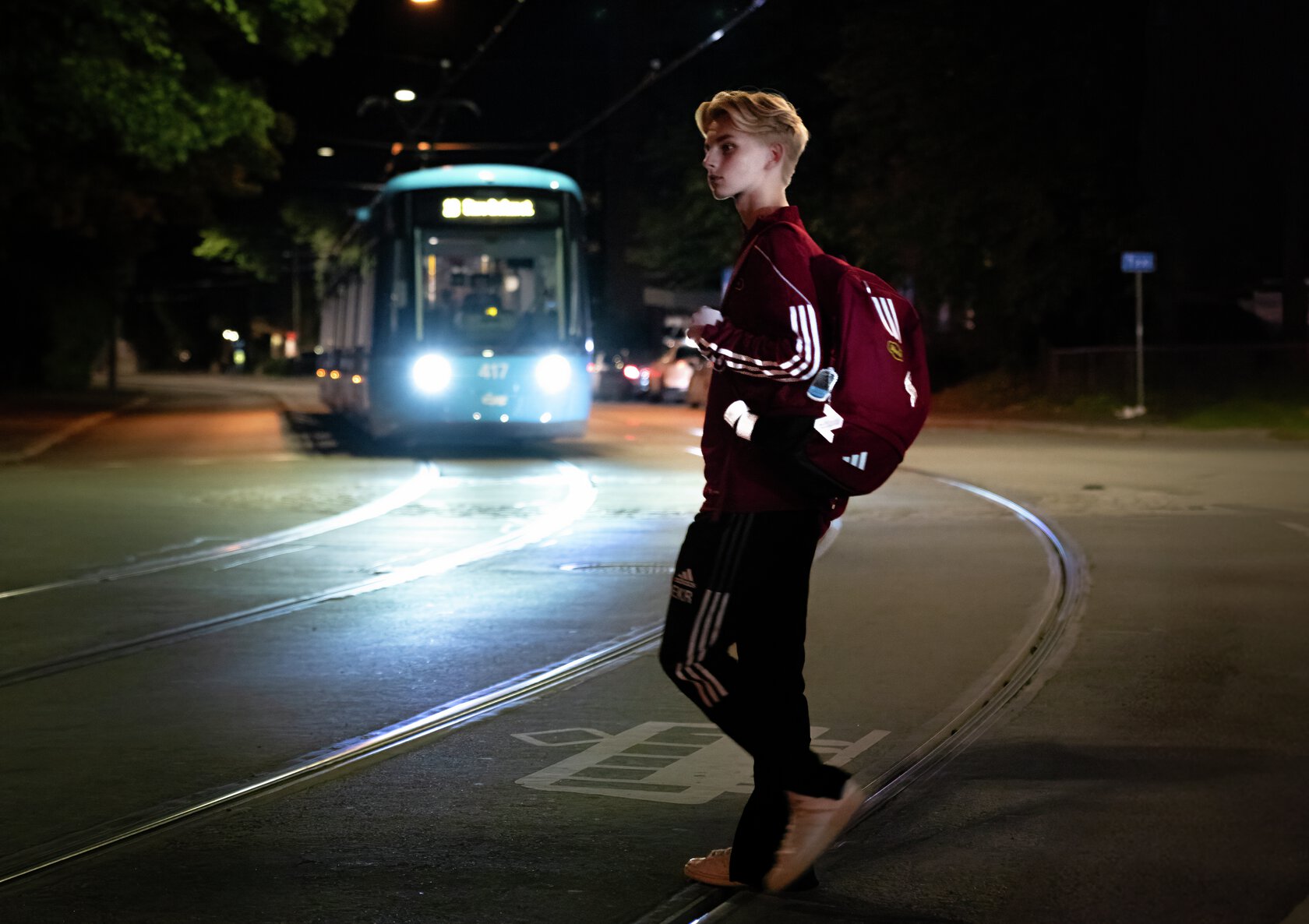Nattestid  trikk kjører mot gutt med reflekser på vei over sporet. Foto.