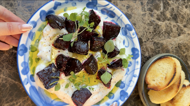 Ovnsbakte rødbeter på kremet pisket ricotta med friske urter, olivenolje og ristede crostini på en blå keramisk tallerken.