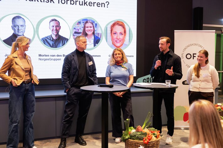 Gruppe mennesker presenterer på scenen med fargerik, sirkulær grafikk bak seg som viser forskjellige ikoner.
