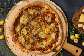 Oversiktsbilde av en rund pizza med forskjellige toppinger på en mørk bakgrunn, omgitt av ingredienser.